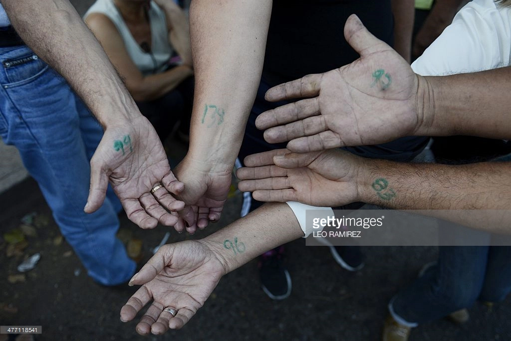 
Những người đàn ông khoe cánh tay được đánh số của mình trong khi chờ đợi siêu thị mở cửa. Ảnh: Leo RAMIREZ/ AFP
