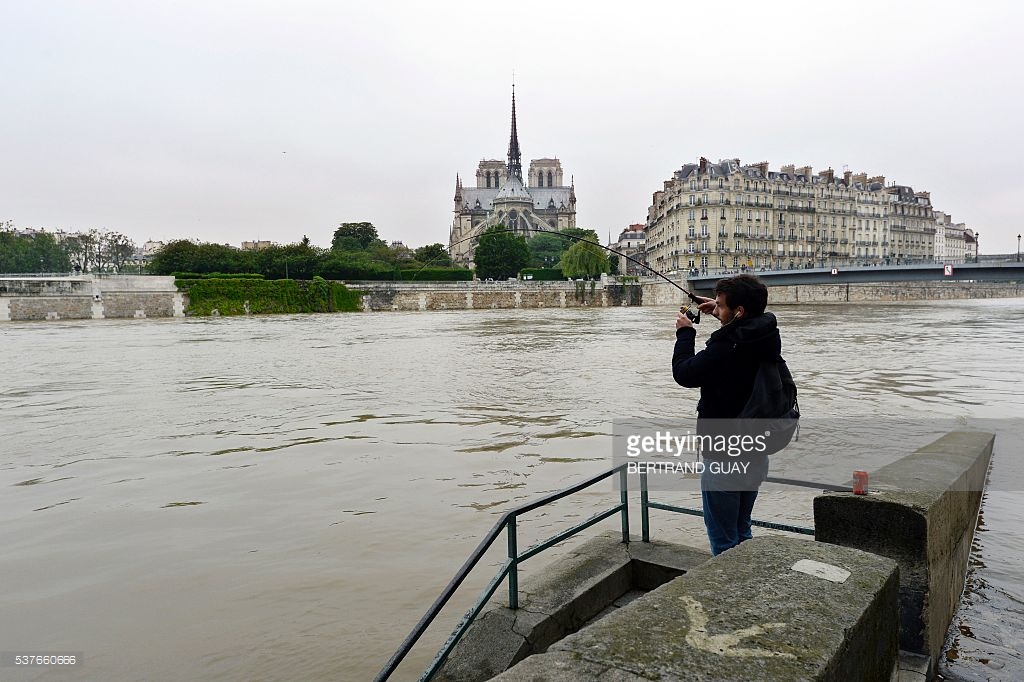 
Một anh chàng tranh thủ câu cá lúc nước sông dâng cao. Ảnh: Bertrand Guay/ AFP
