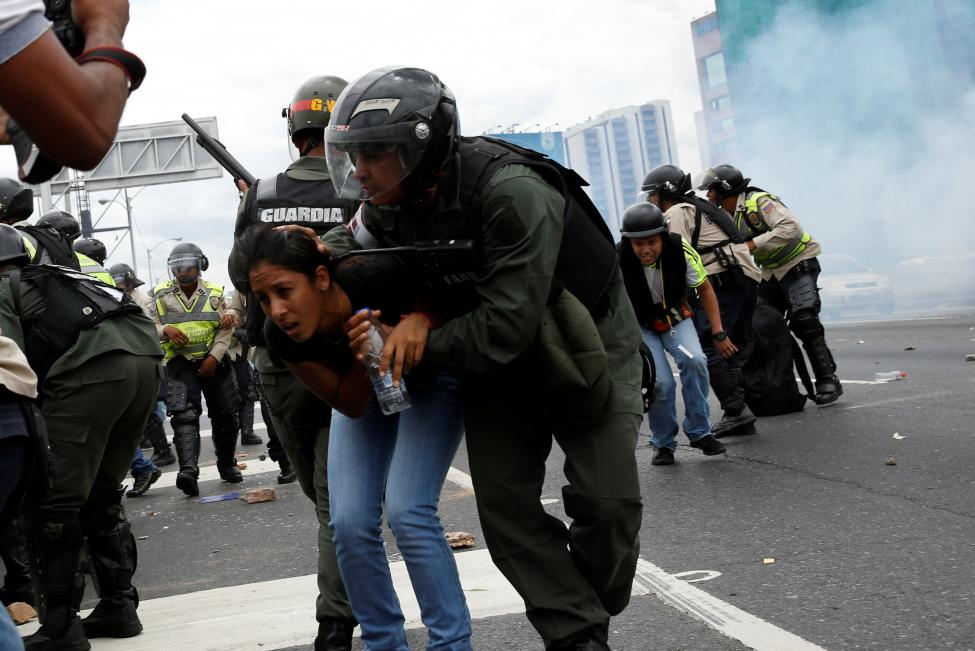 
Một phụ nữ được thành viên lực lượng Vệ binh Quốc gia Venezuela đưa khỏi khu vực bị ảnh hưởng bởi hơi cay. Những người biểu tình muốn xông vào Ủy ban Bầu cử Quốc gia nhưng bị ngăn chặn. Ảnh: Reuters
