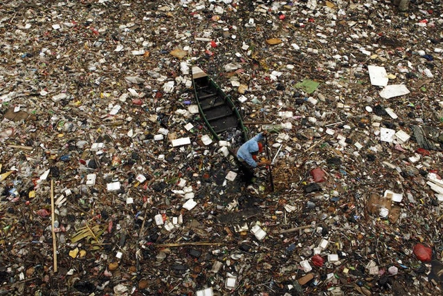 Một người dân đang nhặt nhạnh chai lọ giữa đống rác lềnh bềnh trên 1 dòng sông ở Jakarta, Indonesia.