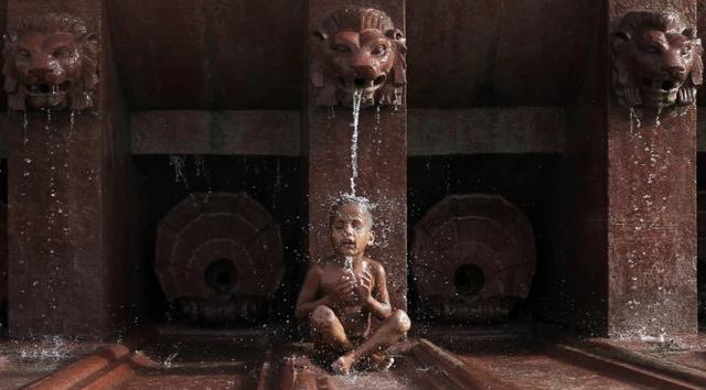Cậu bé Ấn Độ ngồi dưới vòi nước để giải nhiệt ở New Delhi - Ảnh: Reuters