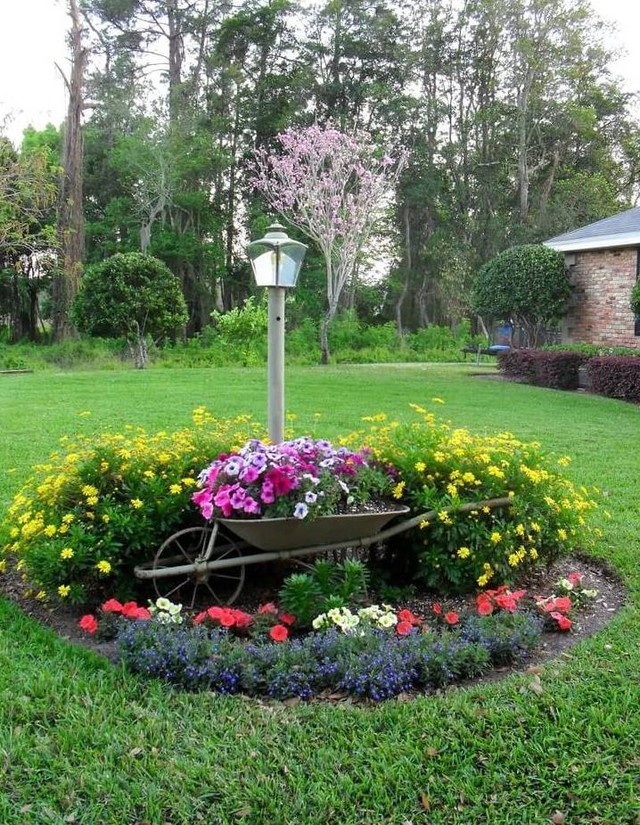 Một góc vườn lãng mạn với hoa lá bao quanh chiếc xe cút kít.