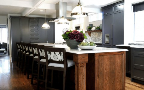 Tủ lạnh màu đen và tủ bếp màu đen phối hợp cùng đảo bếp bằng gỗ và hàng ghế duyên dáng là tâm điểm của căn bếp.